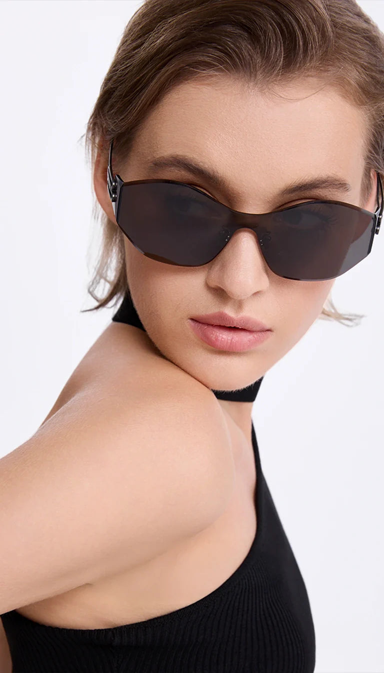 A woman wears asymmetric shield sunglasses paired with a black one-shoulder top, highlighting the eyewear's avant-garde design and ability to elevate minimalist fashion.