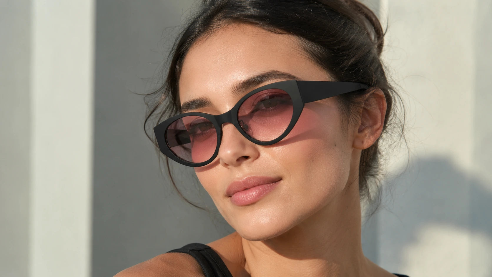 A close-up of a woman wearing BAPORSSA Lyra black cat-eye sunglasses
with soft pink gradient lenses, highlighting the elegant and bold frame
shape