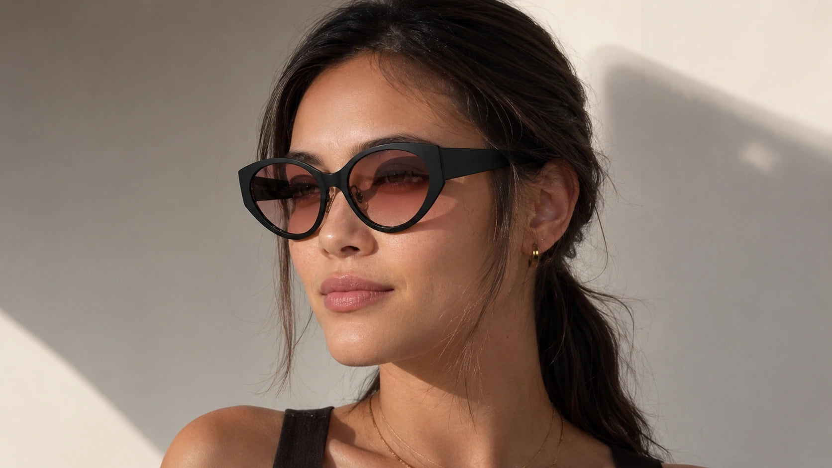 Portrait of a woman wearing Lyra cat-eye sunglasses by BAPORSSA,
featuring modern black frames and rosy tinted lenses in warm natural
sunlight