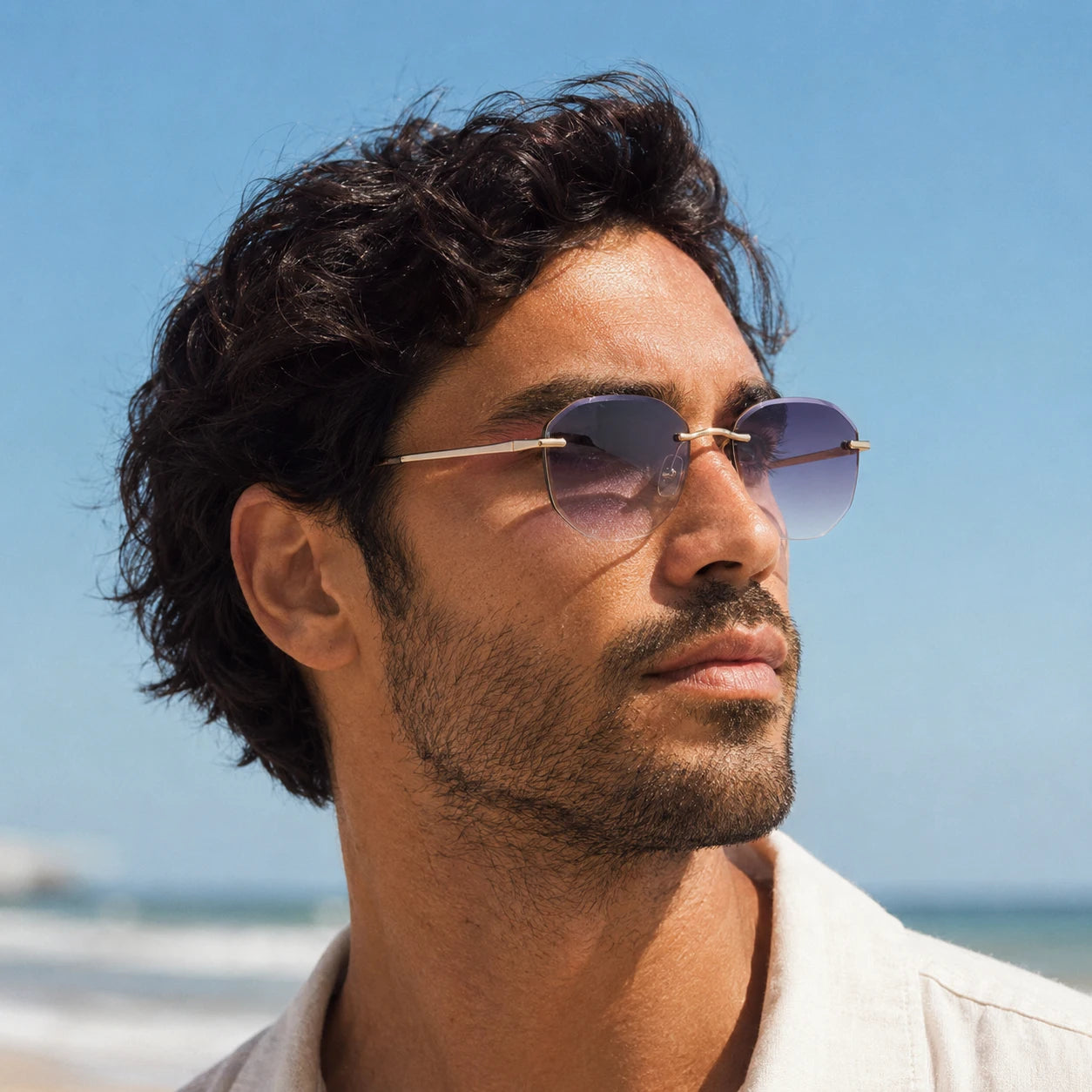 Male model wearing Backbone rimless sunglasses with purple gradient lenses in bright beach sunlight