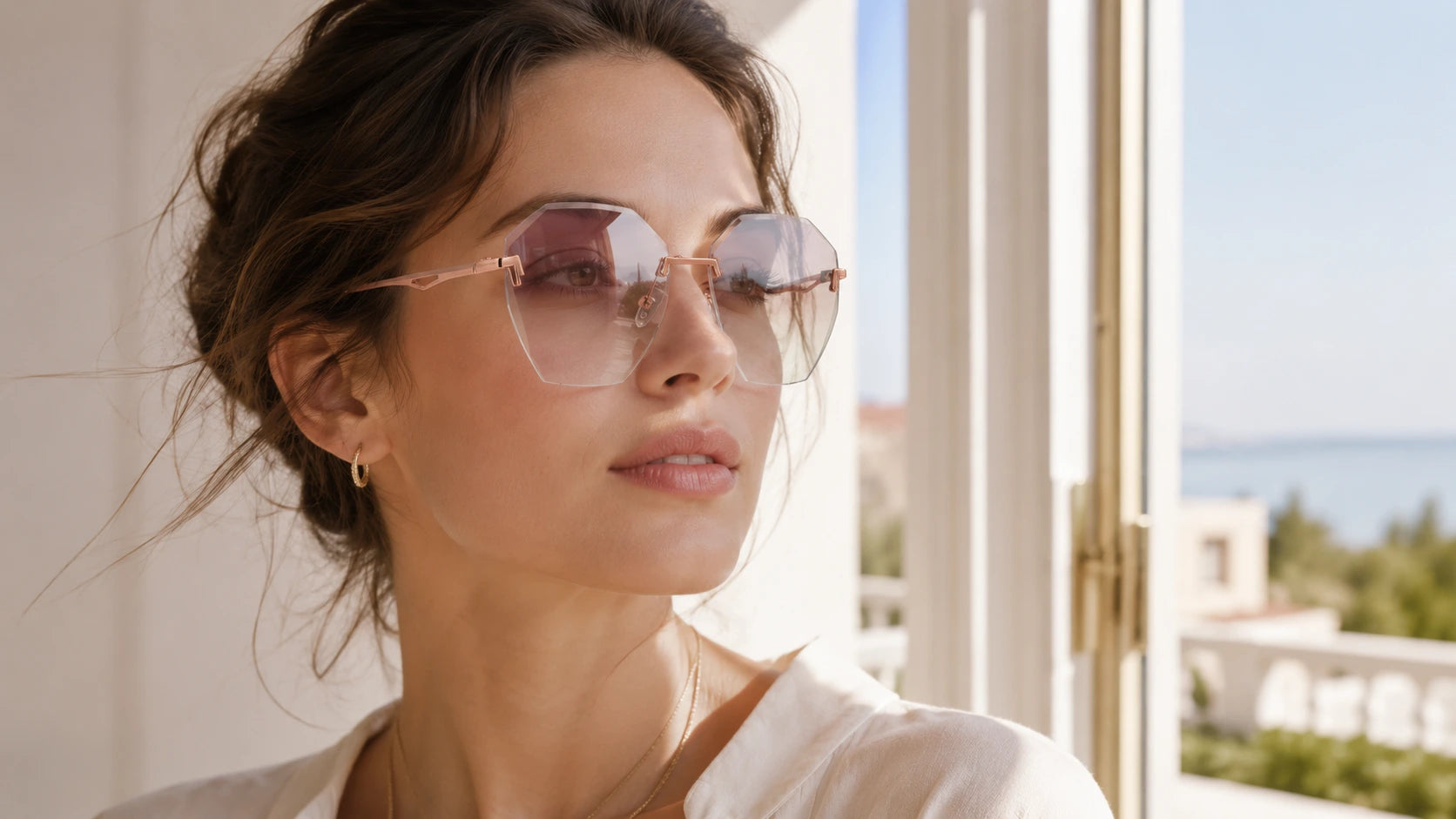 Woman wearing rimless oversized polygon sunglasses with soft tea gradient lenses, rose-gold metal bridge, and clear nose pads near a bright window with outdoor travel light.