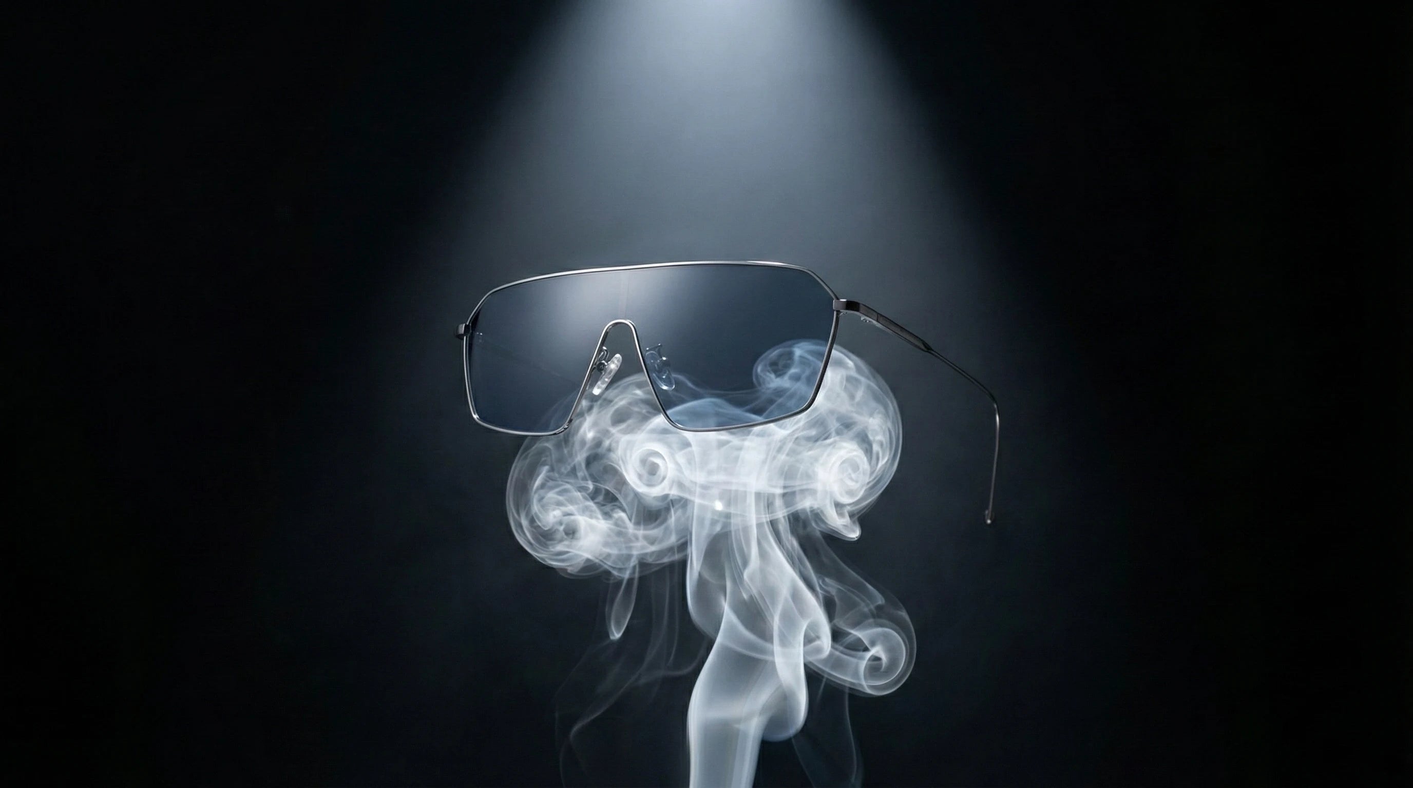 The titanium sunglasses are resting on top of a rising curl of smoke in a dark studio. The smoke supports the glasses, emphasizing extreme lightness.