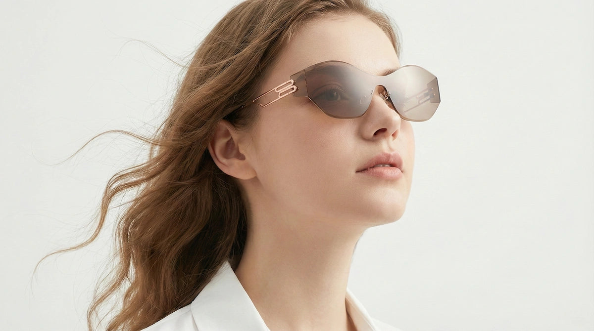 A woman with flowing hair wears modern, rose-gold framed sunglasses against a clean white background.