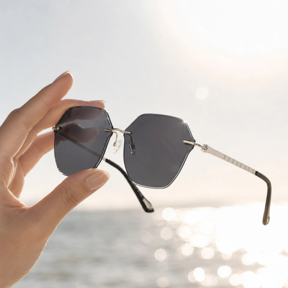 Hand holding rimless dark polarized sunglasses toward strong sunlight over reflective water, showing reduced glare and calmer outdoor vision.