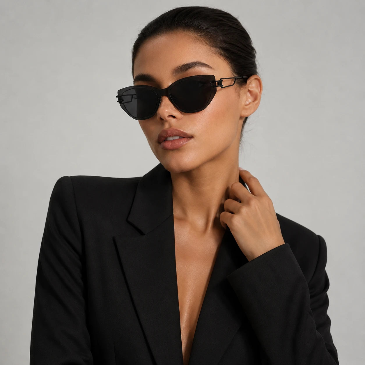 A studio editorial portrait of a woman in a black blazer looking away, wearing Baporssa Edge avant-garde cat-eye metal sunglasses.