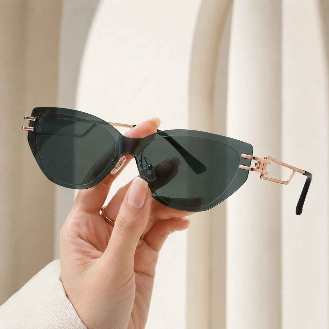 A close-up shot of a hand holding Baporssa Edge rimless geometric sunglasses, highlighting the translucent dark green lens cut and hollow-out gold temple structure.