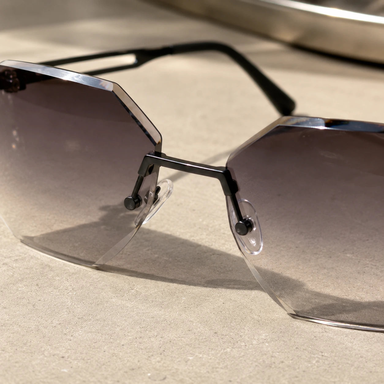 A detailed macro shot of Baporssa Glow sunglasses, highlighting the sleek black metal nose bridge, clear nose pads, and the polished diamond-cut edges of the lenses.
