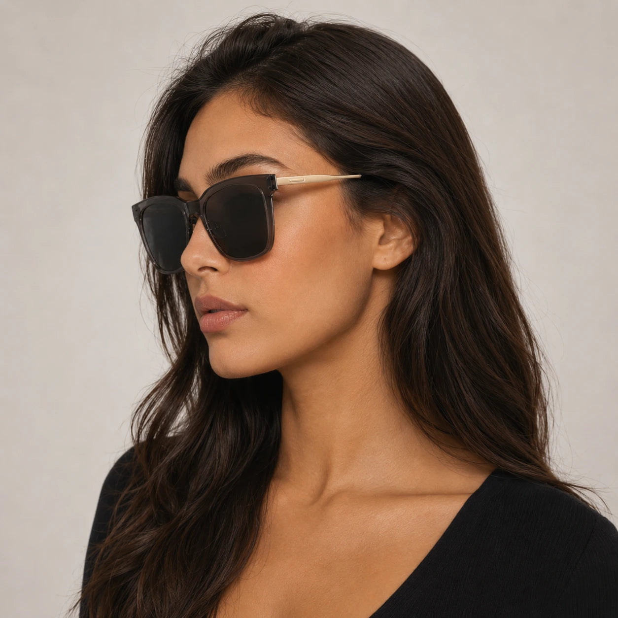 Side profile of a woman wearing Baporssa Halo sunglasses, highlighting the transparent grey frame and the slim gold metal temple arm.