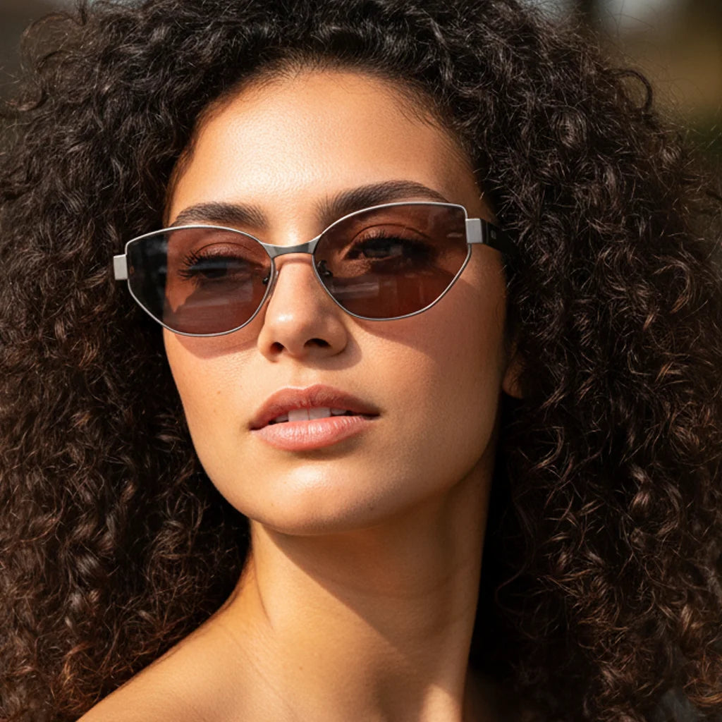Extreme close-up of woman with curly hair wearing lightweight titanium cat-eye sunglasses with visible tea-colored lenses