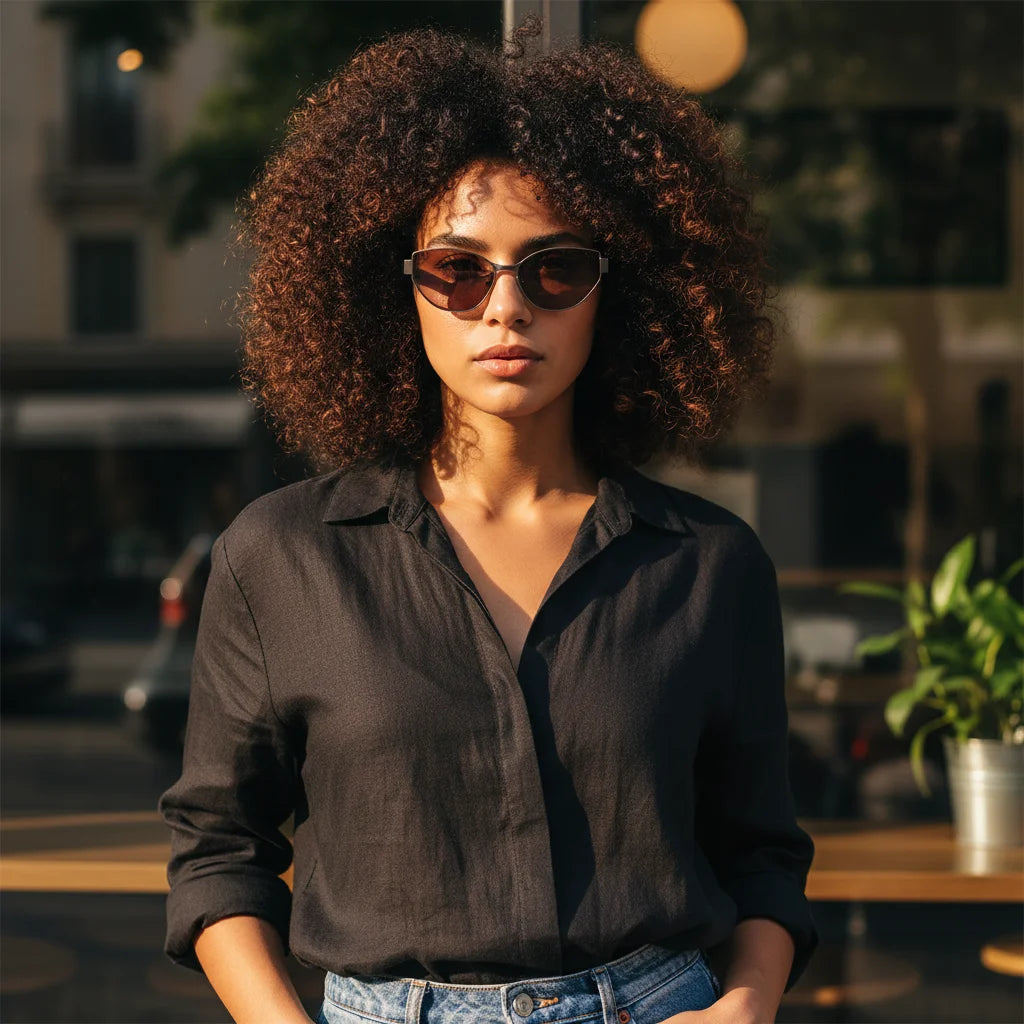 Curly-haired woman wearing silver titanium cat-eye sunglasses outdoors, styled with black shirt and jeans