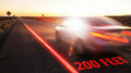A speeding car (motion-blurred) travels on a desert highway at sunset; "200 FEET" is marked on the road, and traffic signs are visible in the distance, evoking a sense of speed and open-road travel.
