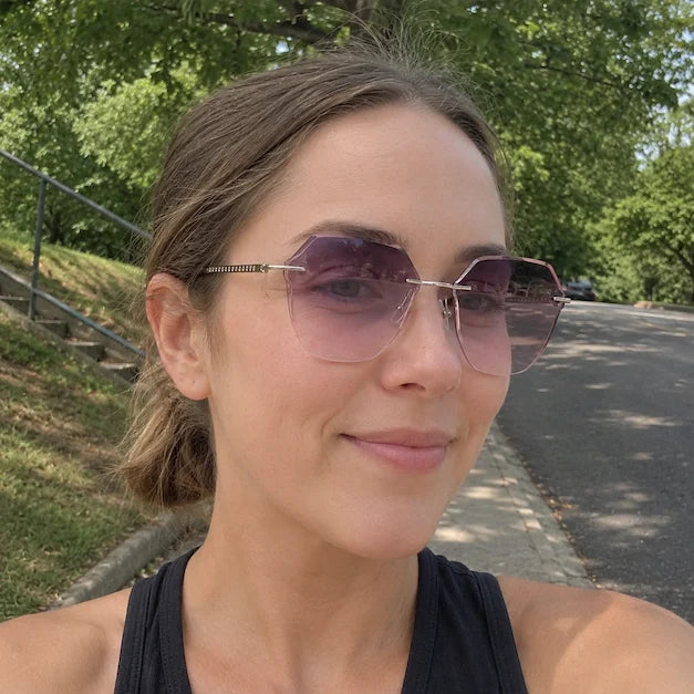 Woman in an outdoor selfie wearing lightweight pink gradient rimless sunglasses.
