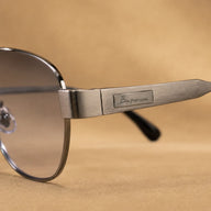 Close-up of BAPORSSA Aurelia gunmetal sunglasses showing brushed metal temple, logo plate, hinge detail, and smoke lens edge