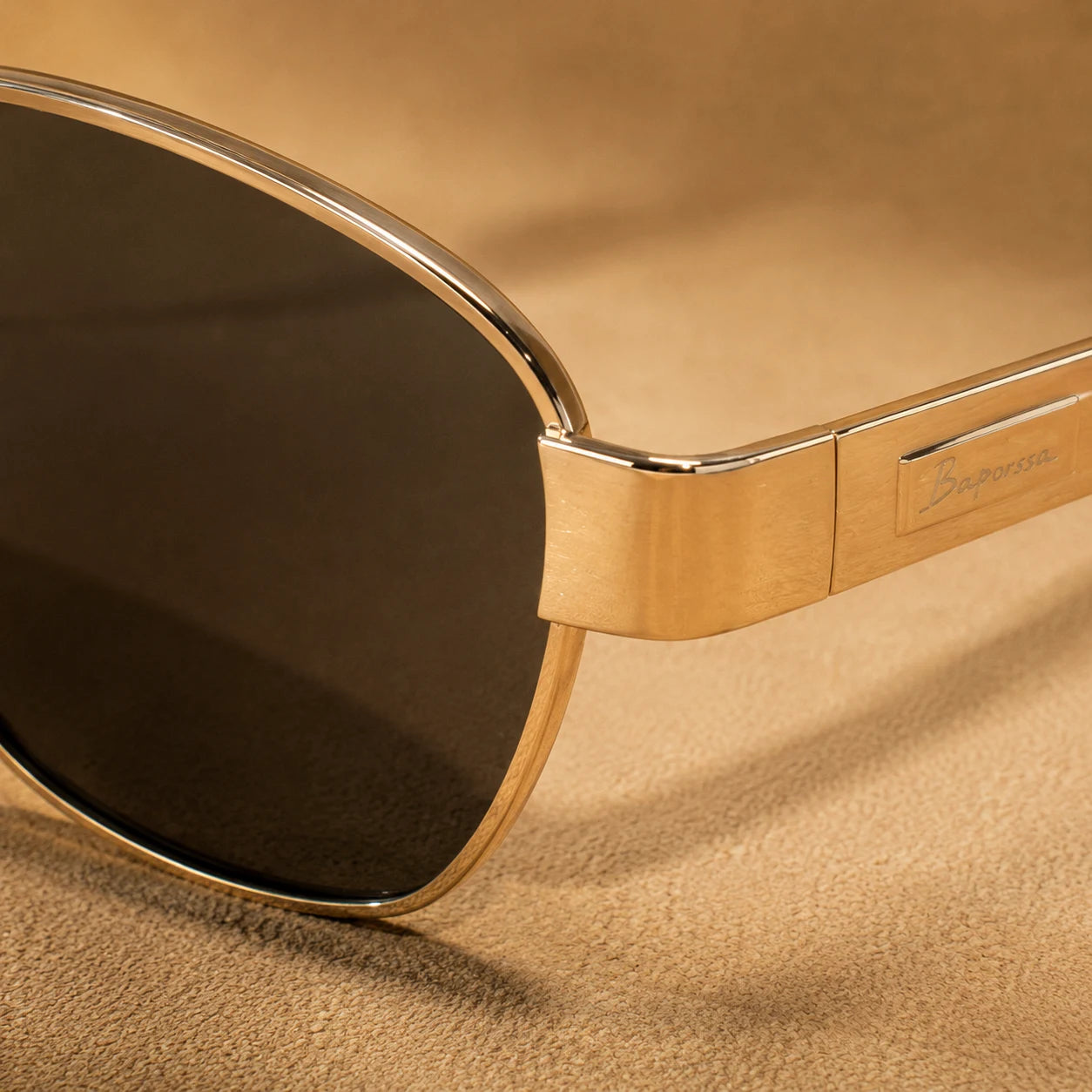 Close-up of BAPORSSA Aurelia sunglasses showing gold metal rim, smoke nylon lens, hinge detail, and engraved temple logo