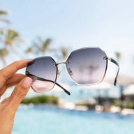 Hand holding BAPORSSA Contour rimless sunglasses with oversized geometric gradient lenses by a sunny poolside setting