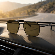 BAPORSSA Shift dark lens sunglasses placed on a car dashboard with a sunny coastal road in the background