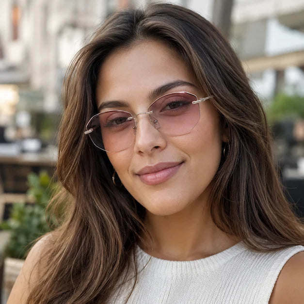 Woman wearing pink gradient rimless sunglasses in natural daylight on a city street.