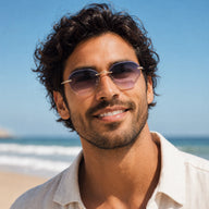 Smiling male model wearing Backbone sunglasses with slim gold temples and gradient lenses by the ocean