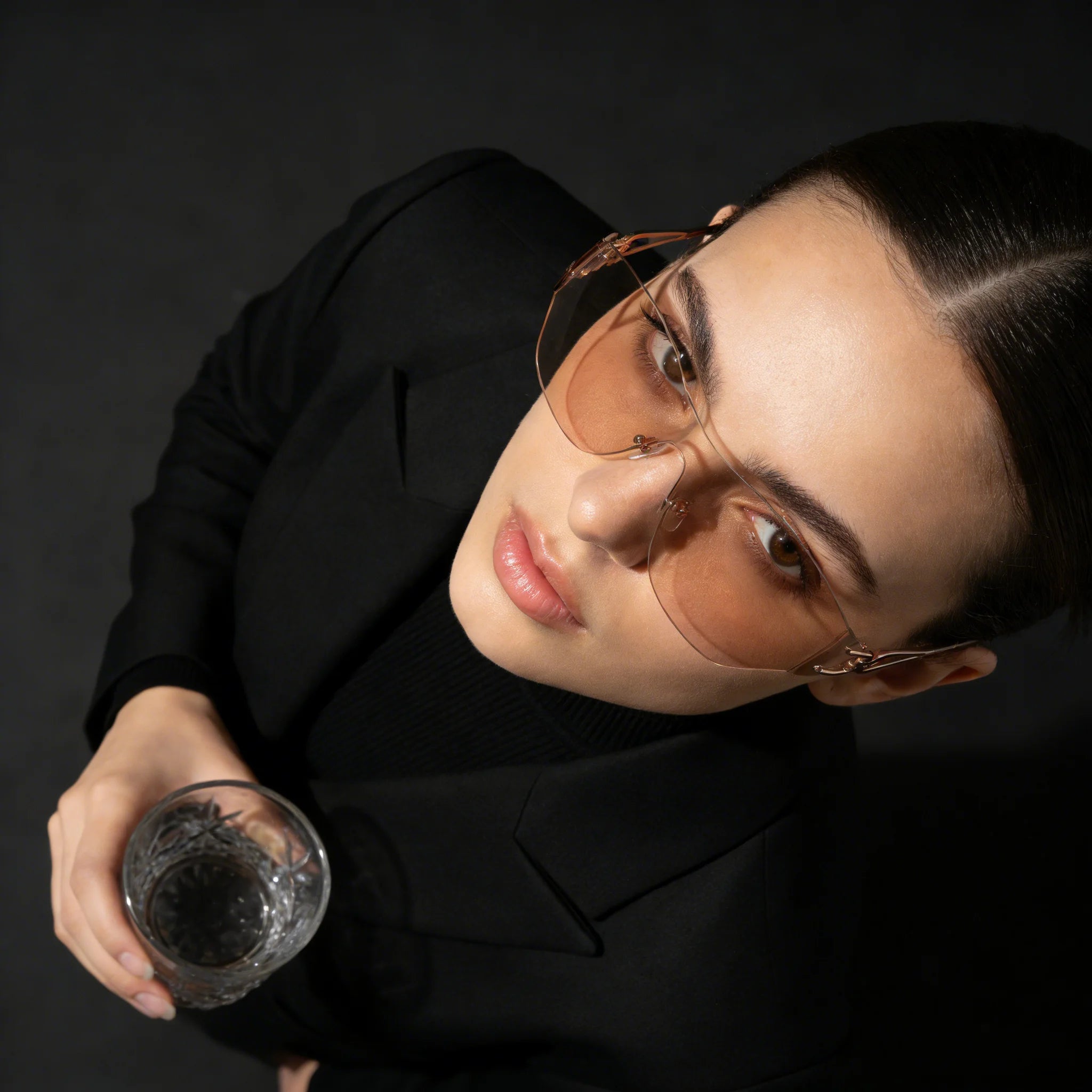 Woman wearing sunglasses and holding a glass against a dark background
