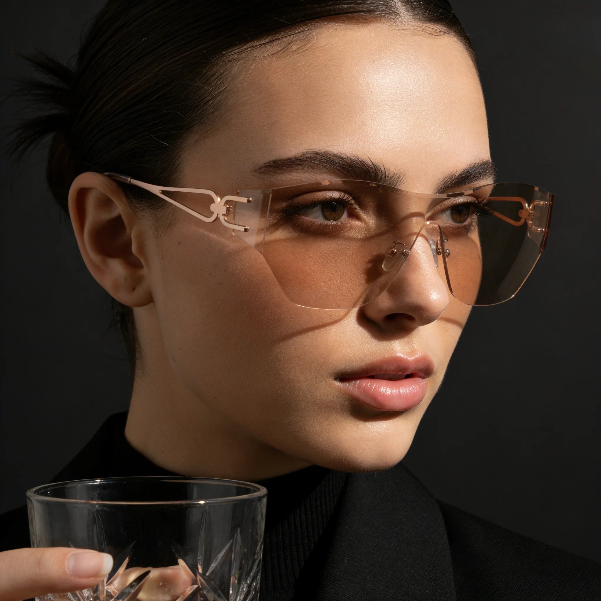 Woman wearing sunglasses holding a glass against a dark background