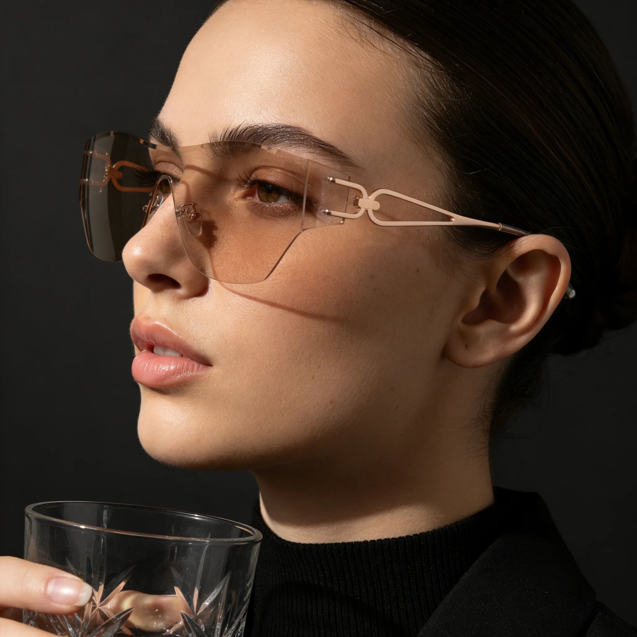 Woman wearing futuristic eyewear holding a glass against a dark background
