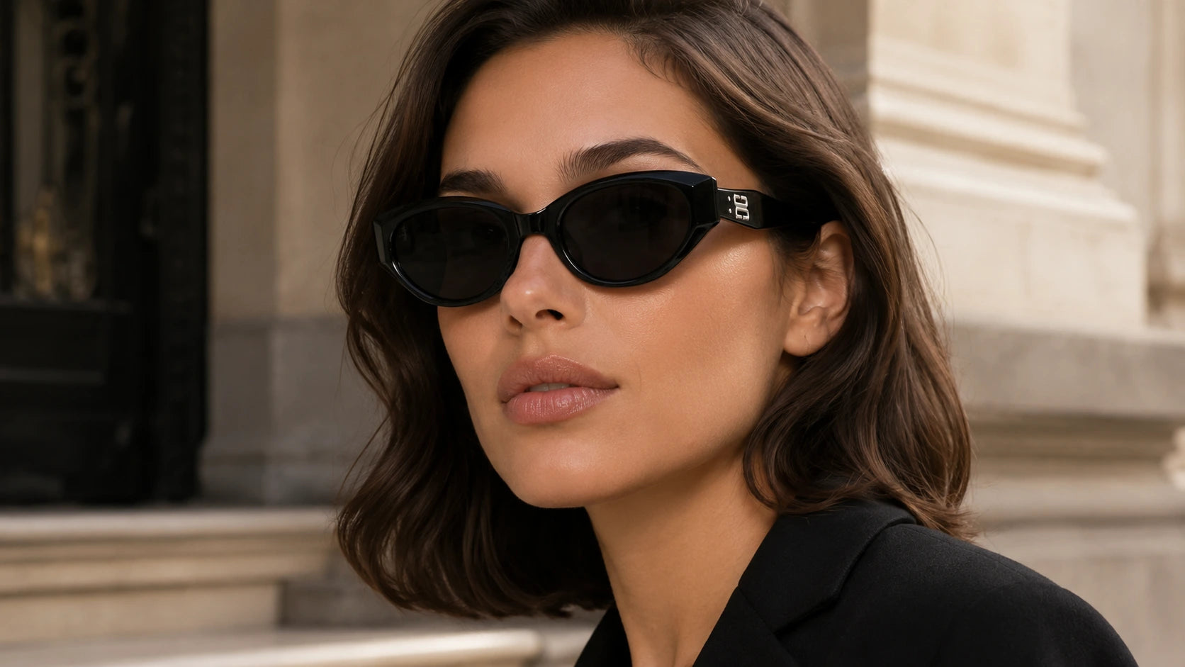 Woman wearing black Coco soft cat-eye sunglasses with dark nylon lenses and visible temple hinge detail in a refined everyday editorial setting.