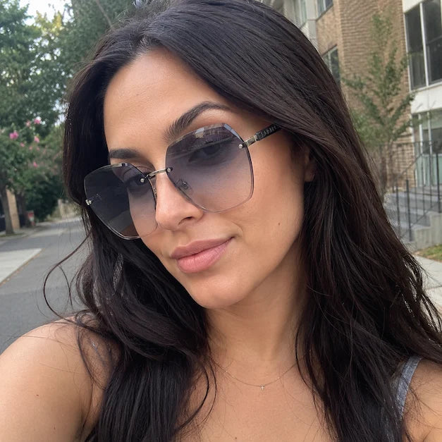 Woman taking a casual street selfie wearing gray gradient oversized rimless sunglasses.