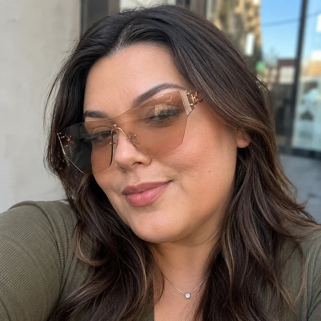 Woman taking a casual street selfie wearing tea-colored rimless sunglasses.