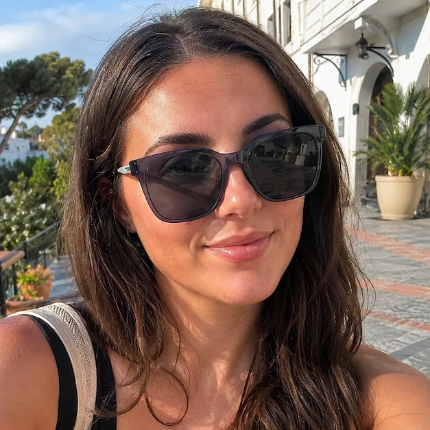 Woman wearing purple square sunglasses in bright sunlight during a travel day.