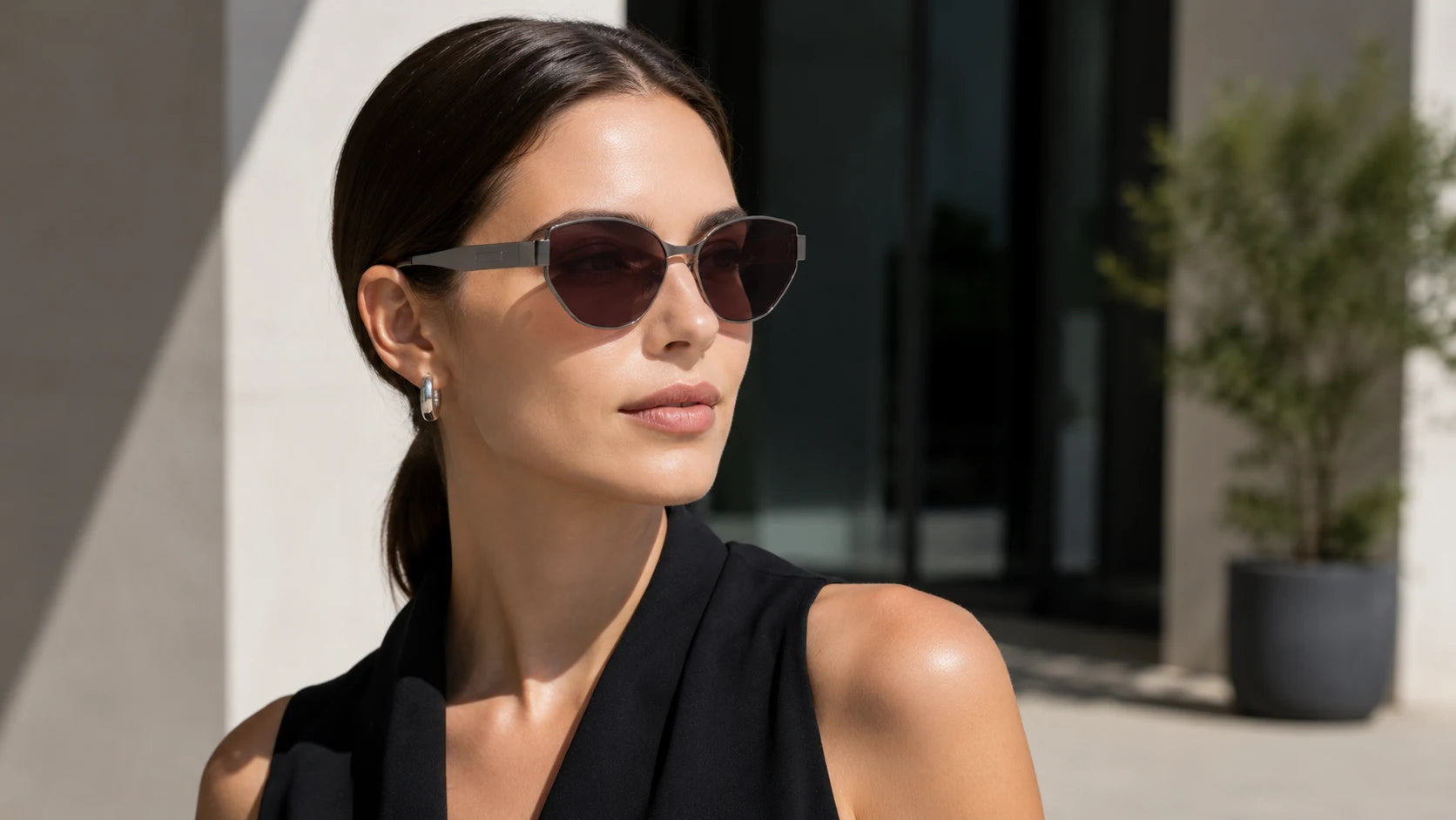 Woman wearing Onyx polarized titanium cat-eye sunglasses with claret dark lenses, slim metal rim, adjustable nose pads, and lightweight metal temples in bright city sunlight.