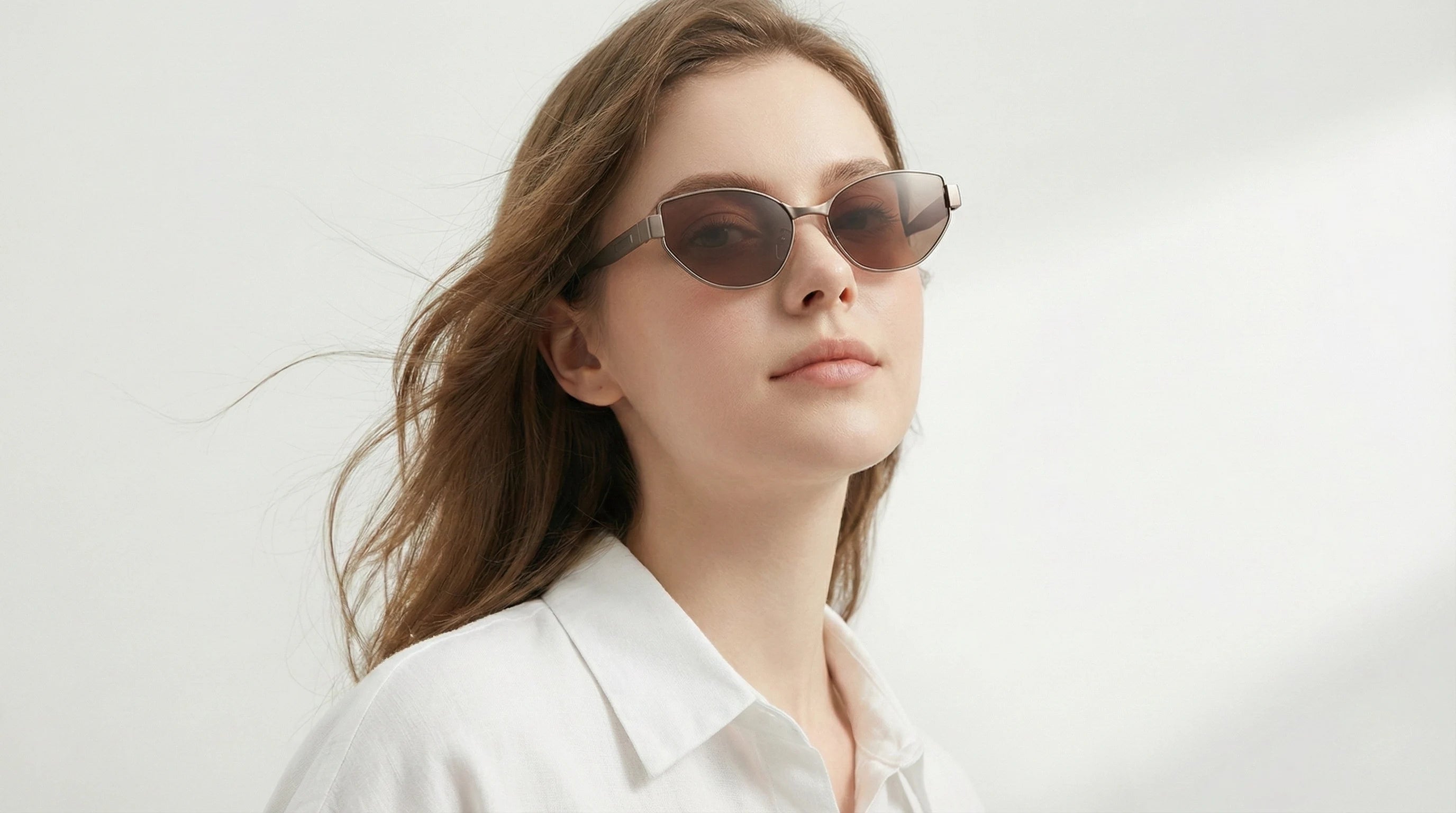A woman wears oval cat-eye sunglasses with a white shirt, showcasing the style’s blend of modern sophistication and all-day comfort.