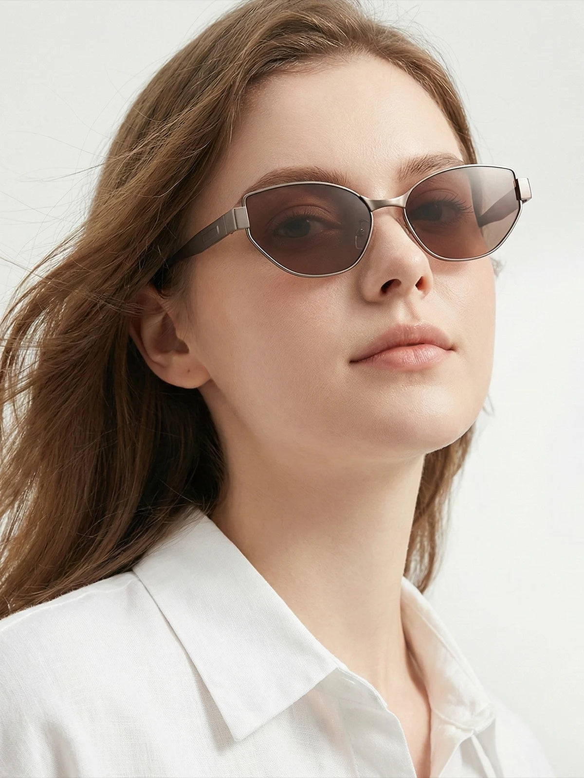 A woman wears oval cat-eye sunglasses with a white shirt, showcasing the style’s blend of modern sophistication and all-day comfort.
