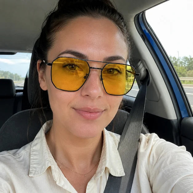 Woman taking a car selfie wearing yellow lens sunglasses during a daytime drive.