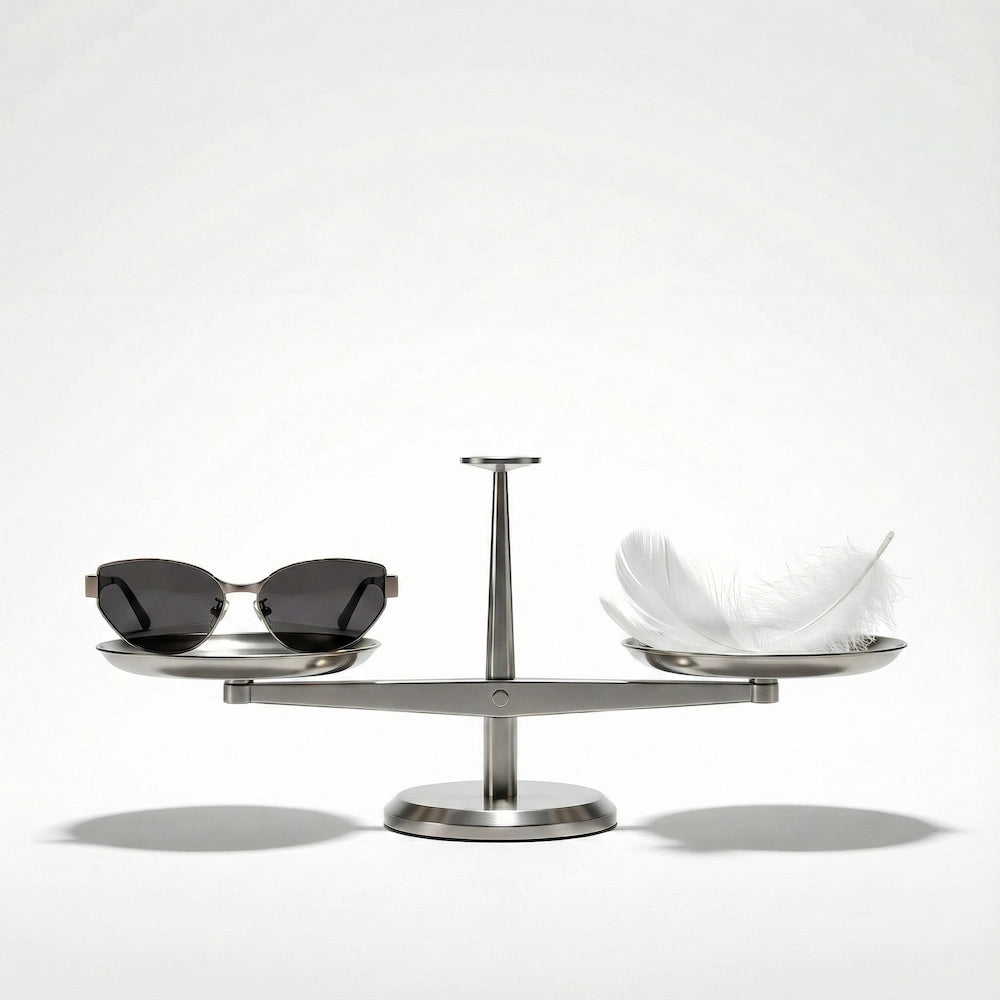 Sunglasses balanced on a scale with a feather, emphasizing the product’s extreme lightness—a key feature for long-wear comfort in premium eyewear.