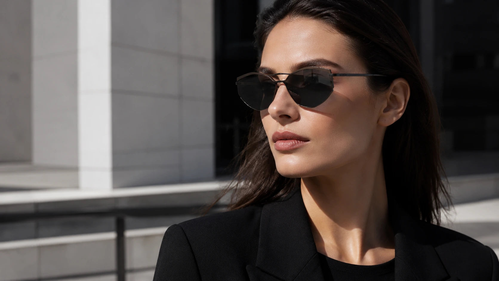 Woman wearing Volt architectural cat-eye sunglasses with black gradient nylon lenses, sharp lifted geometry, slim metal frame, and modern city styling.