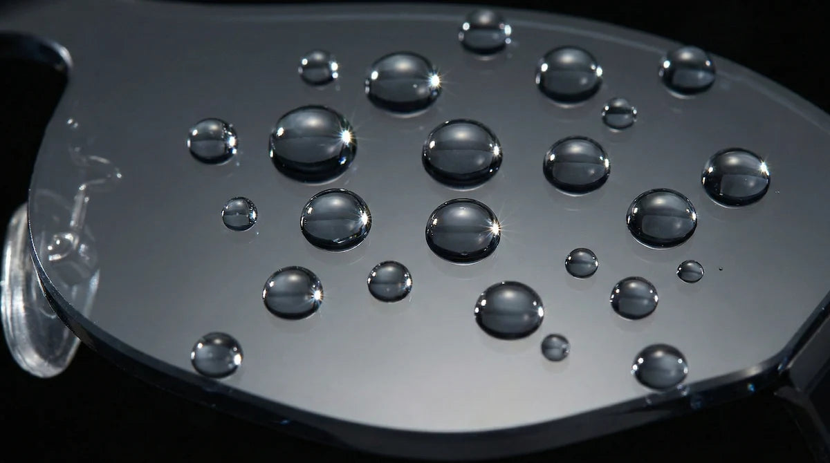 Close-up of spherical water droplets beading up on a dark, non-wetting surface.
