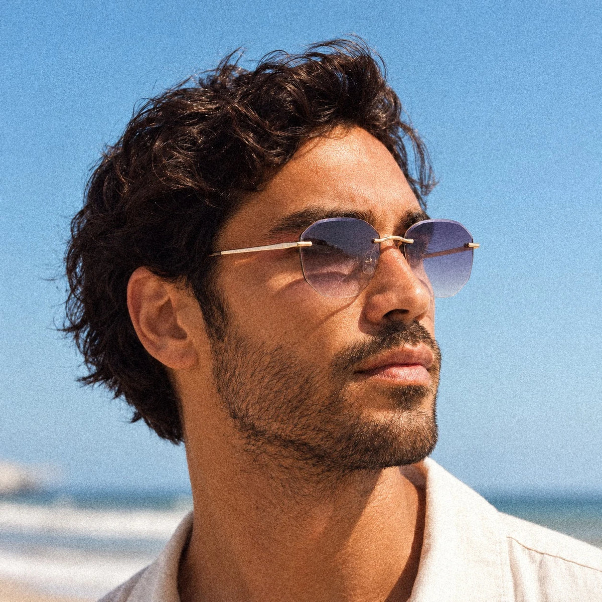 BAPORSSA Backbone rimless sunglasses in Crystal Grey, worn by a model in bright beach sunlight