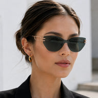 Front portrait of a woman looking directly forward, wearing Baporssa Edge sharp rimless cat-eye sunglasses with dark green lenses and gold hardware.