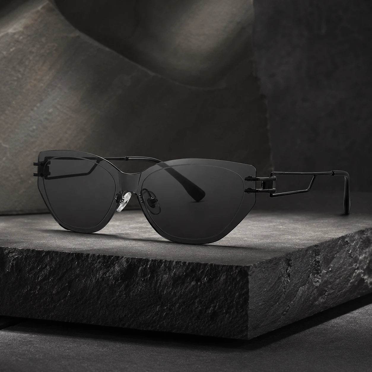 A premium still life shot of Baporssa Edge rimless cat-eye sunglasses with sharp dark lenses and geometric black metal temples, resting on a textured dark stone block.