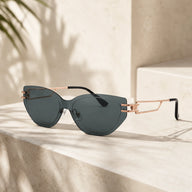 A high-end still life shot of Baporssa Edge rimless cat-eye sunglasses with dark green lenses and rose gold metal temples, resting on a beige stone staircase.