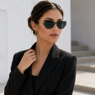 Editorial portrait of a woman in a black blazer looking to the side, wearing Baporssa Edge translucent dark green sunglasses with gold temples.