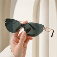 A close-up shot of a hand holding Baporssa Edge rimless geometric sunglasses, highlighting the translucent dark green lens cut and hollow-out gold temple structure.