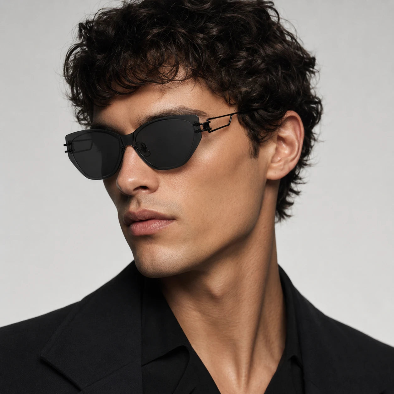 Side profile portrait of a male model with curly hair wearing Baporssa Edge unisex rimless black cat-eye sunglasses with geometric temples.