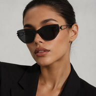 Front close-up portrait of a woman wearing Baporssa Edge black rimless cat-eye sunglasses with sharp geometric lenses, paired with a black blazer.