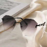 Baporssa Glow rimless designer sunglasses featuring dark grey gradient lenses and hollow black temples, displayed next to a book on a soft white linen fabric.
