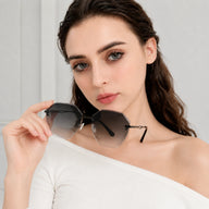 A portrait of a woman holding Baporssa Glow rimless sunglasses with black metal hardware and grey gradient lenses, wearing an off-the-shoulder white top.