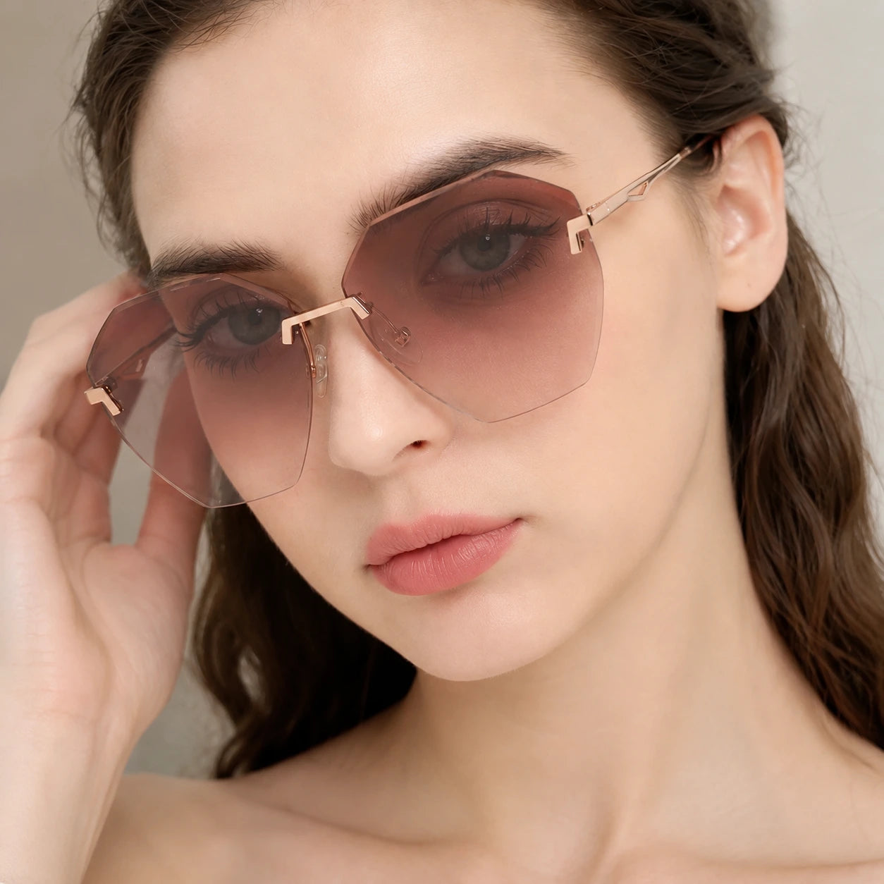 A tight close-up shot of a woman wearing Baporssa Glow oversized rimless sunglasses, showcasing the polygonal cut-edge lenses and subtle rose gold bridge.