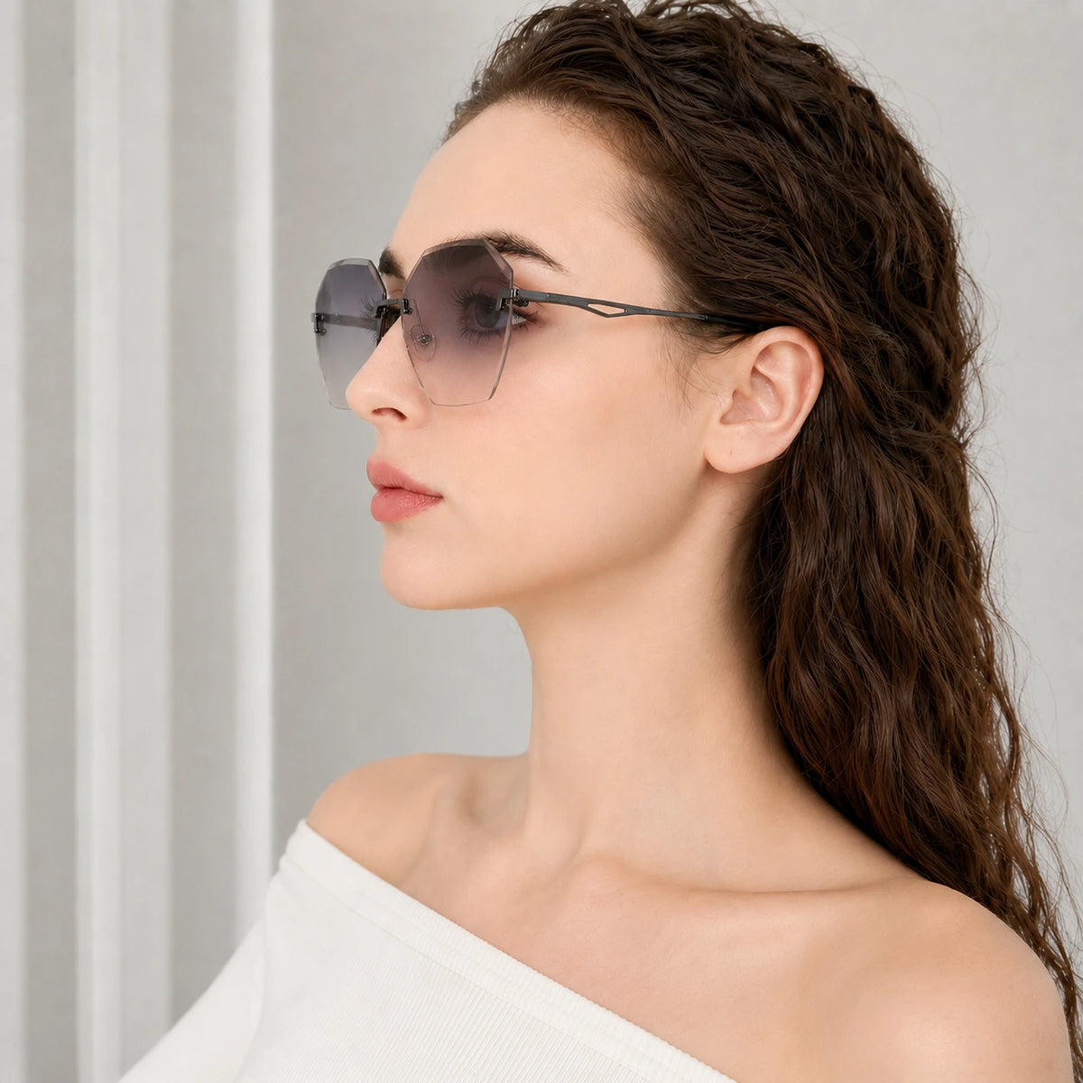 A side profile view of a woman wearing BAPORSSA Glow rimless sunglasses with dark grey gradient polygonal lenses and sleek black metal temples.