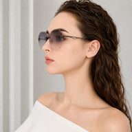 A side profile view of a woman wearing Baporssa Glow rimless sunglasses with dark gray gradient polygonal lenses and sleek black metal temples.