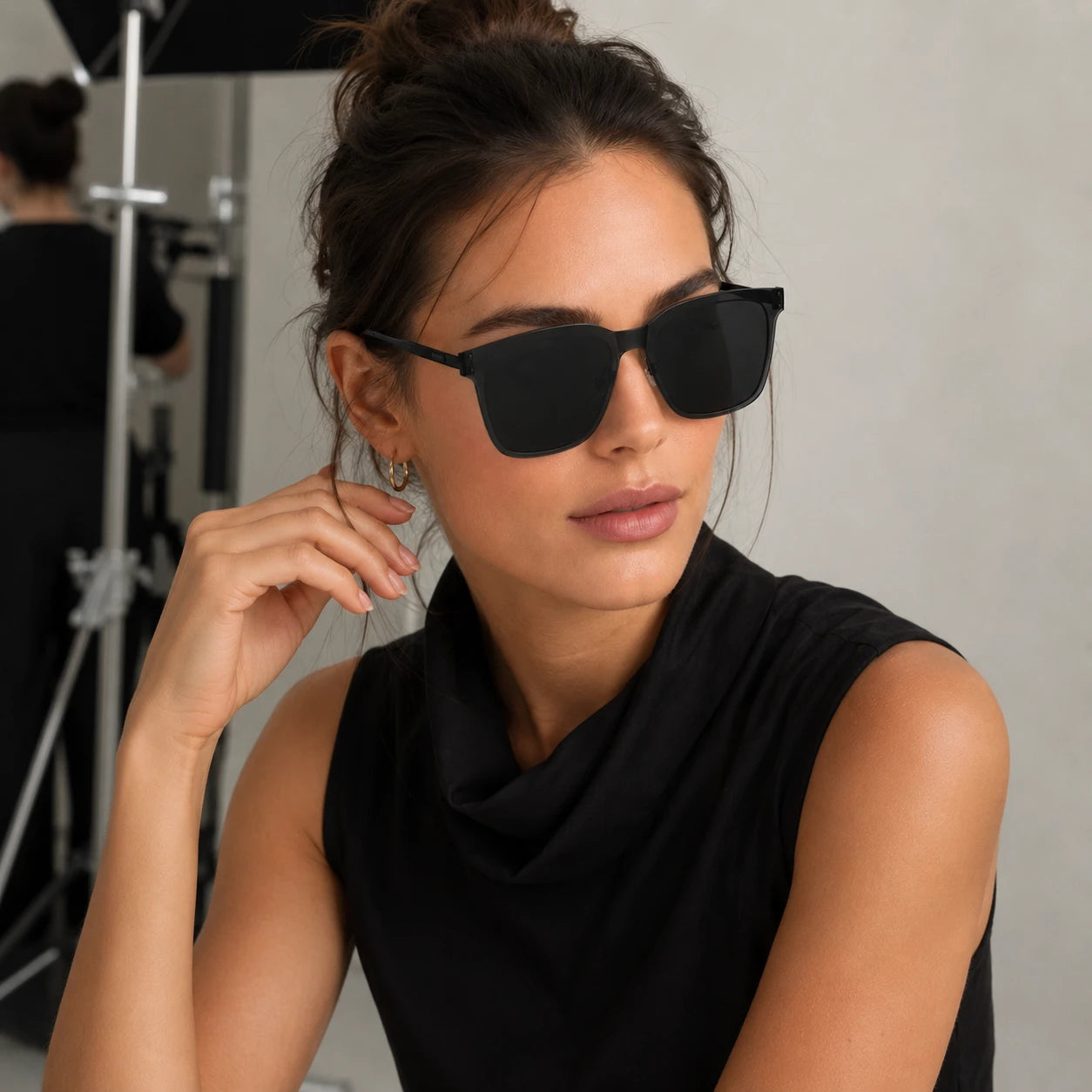 A portrait of a woman looking slightly to the side, wearing Baporssa Halo oversized square sunglasses in classic black with dark lenses.